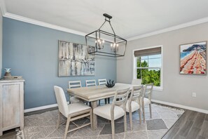 A dining area with a wooden table and chairs, a chandelier, artwork on the walls, and a window with a view. - New Listing! |Beautiful 4 bedroom villa |Private Beach Club |Pickle Ball |Tennis |2 pools |Golf (Pensacola)