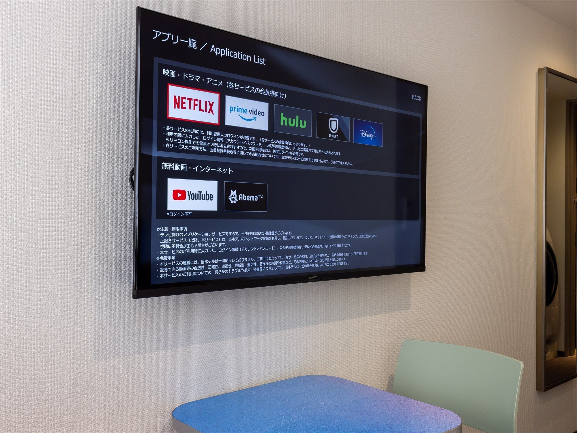 Televisor de pantalla plana montado en la pared mostrando una lista de aplicaciones con logotipos de servicios como Netflix, Hulu y YouTube.