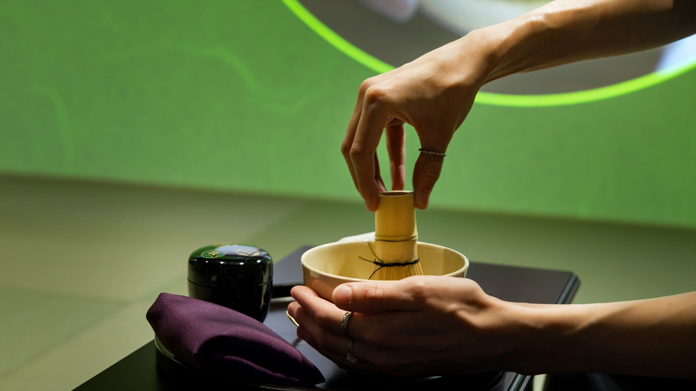 Una persona mezclando una bebida en una taza de cerámica con un batidor de bambú.