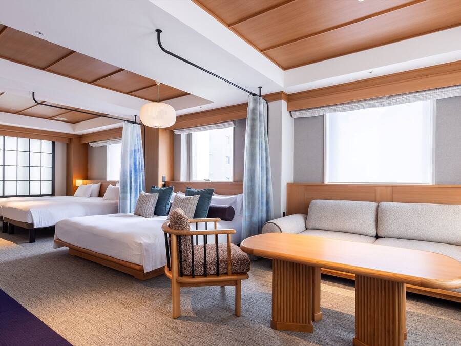 A modern hotel room with two beds, a sofa, a chair, and a table.