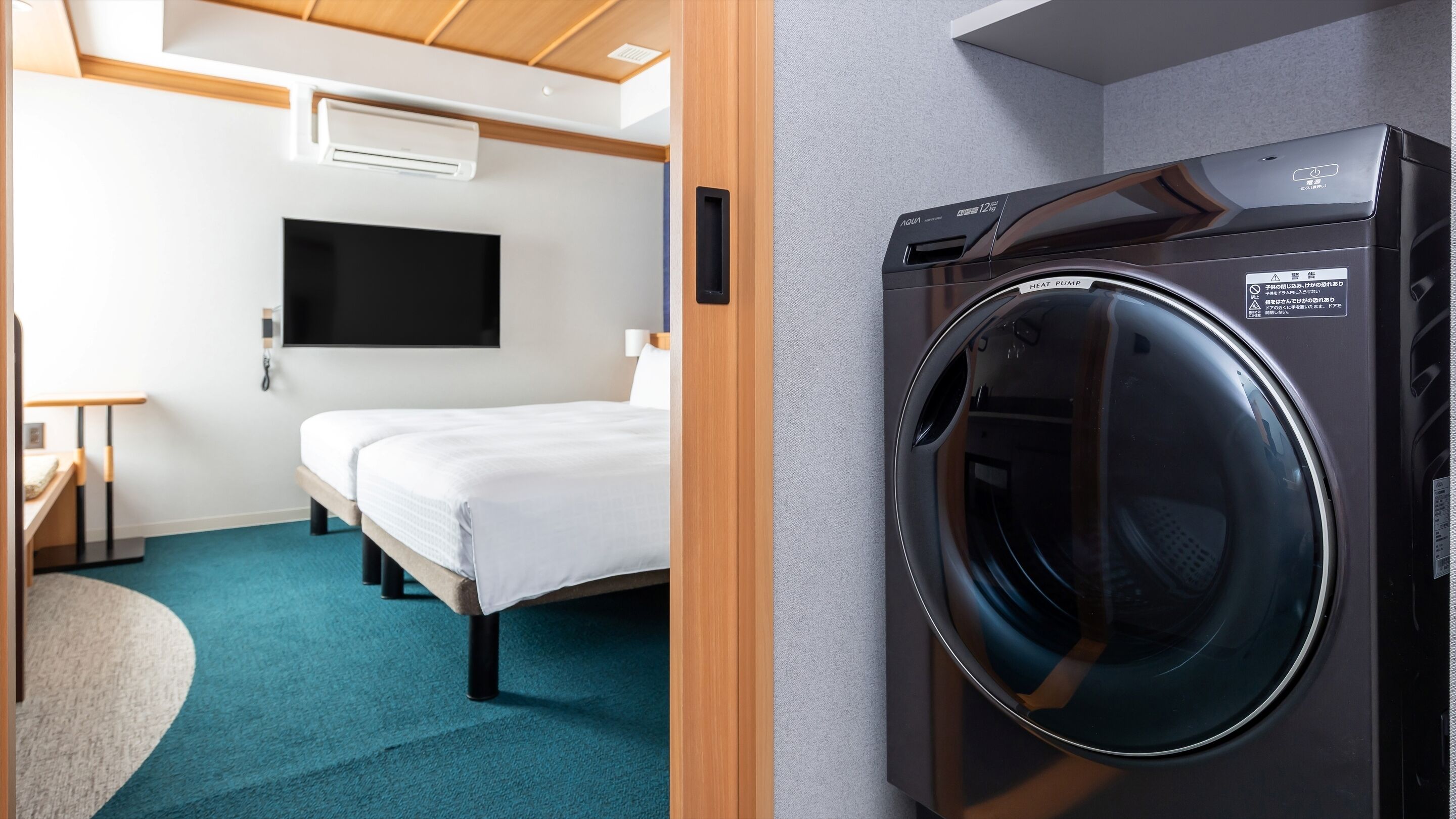 A hotel room with a bed, a TV mounted on the wall, and a washing machine.