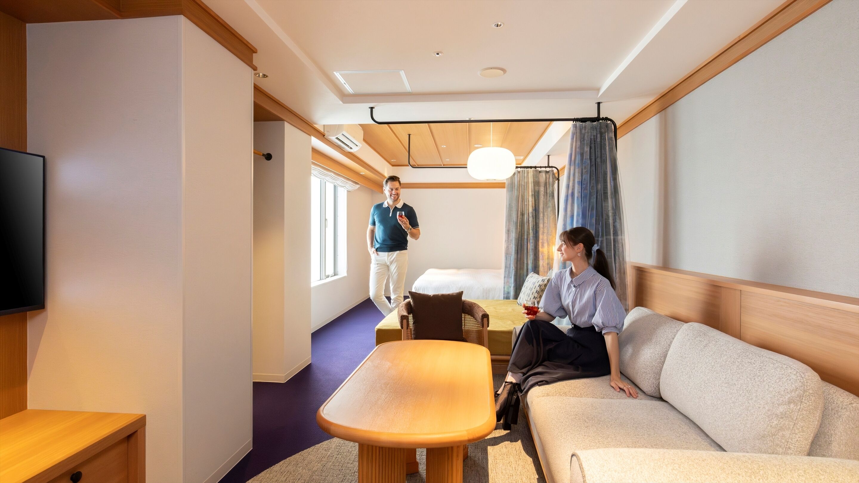 A hotel room with a bed, a sofa, a small table, and a TV.