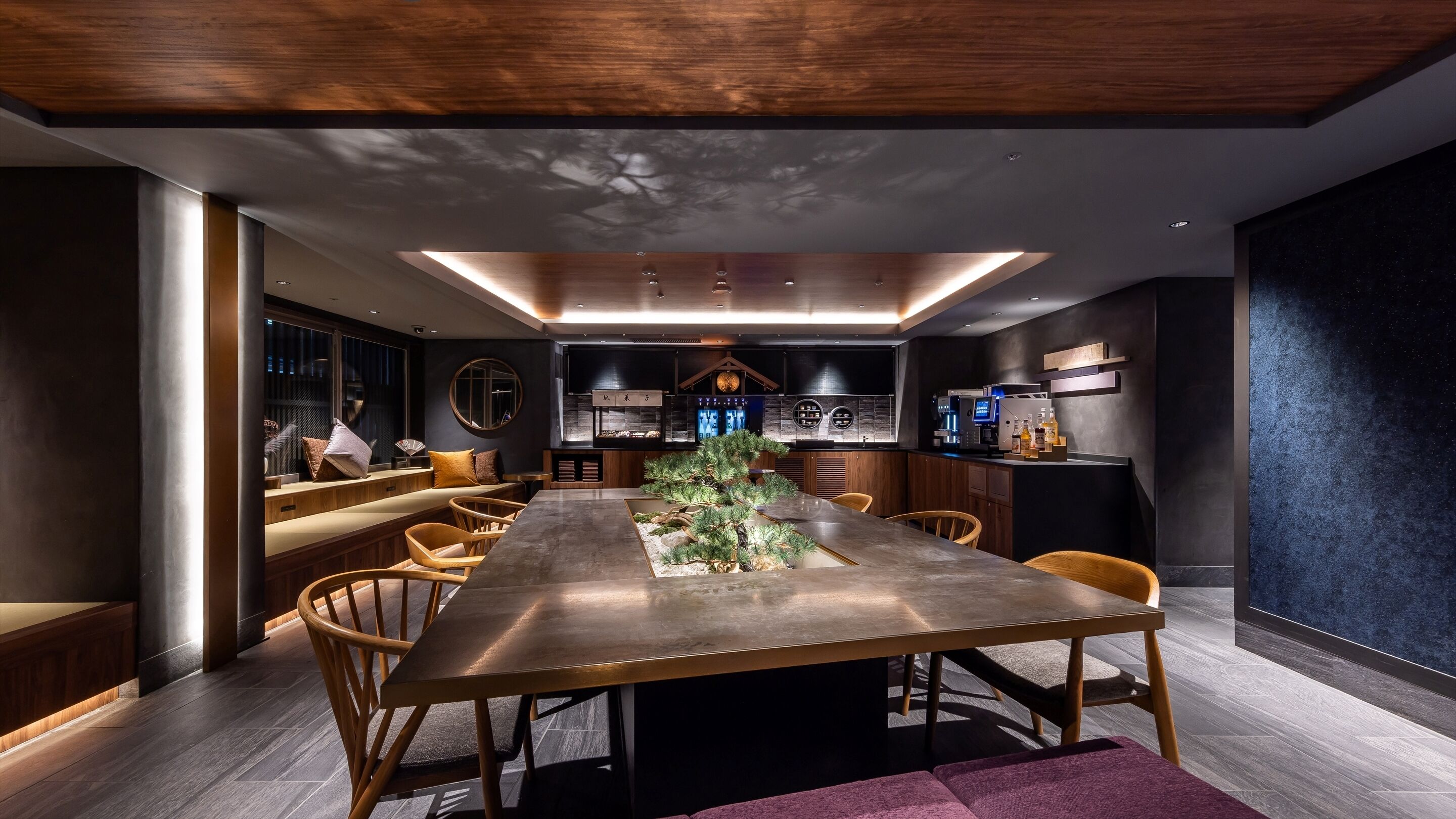 A modern dining area with a long table, wooden chairs, and a central decorative tree.