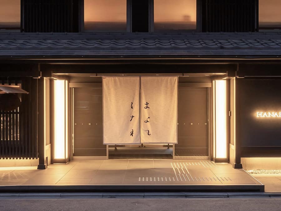 A hotel entrance with a traditional Japanese design, featuring a sliding door with Japanese characters, a sign reading 'HANARE TOKYU STAY', and a modern, illuminated facade.