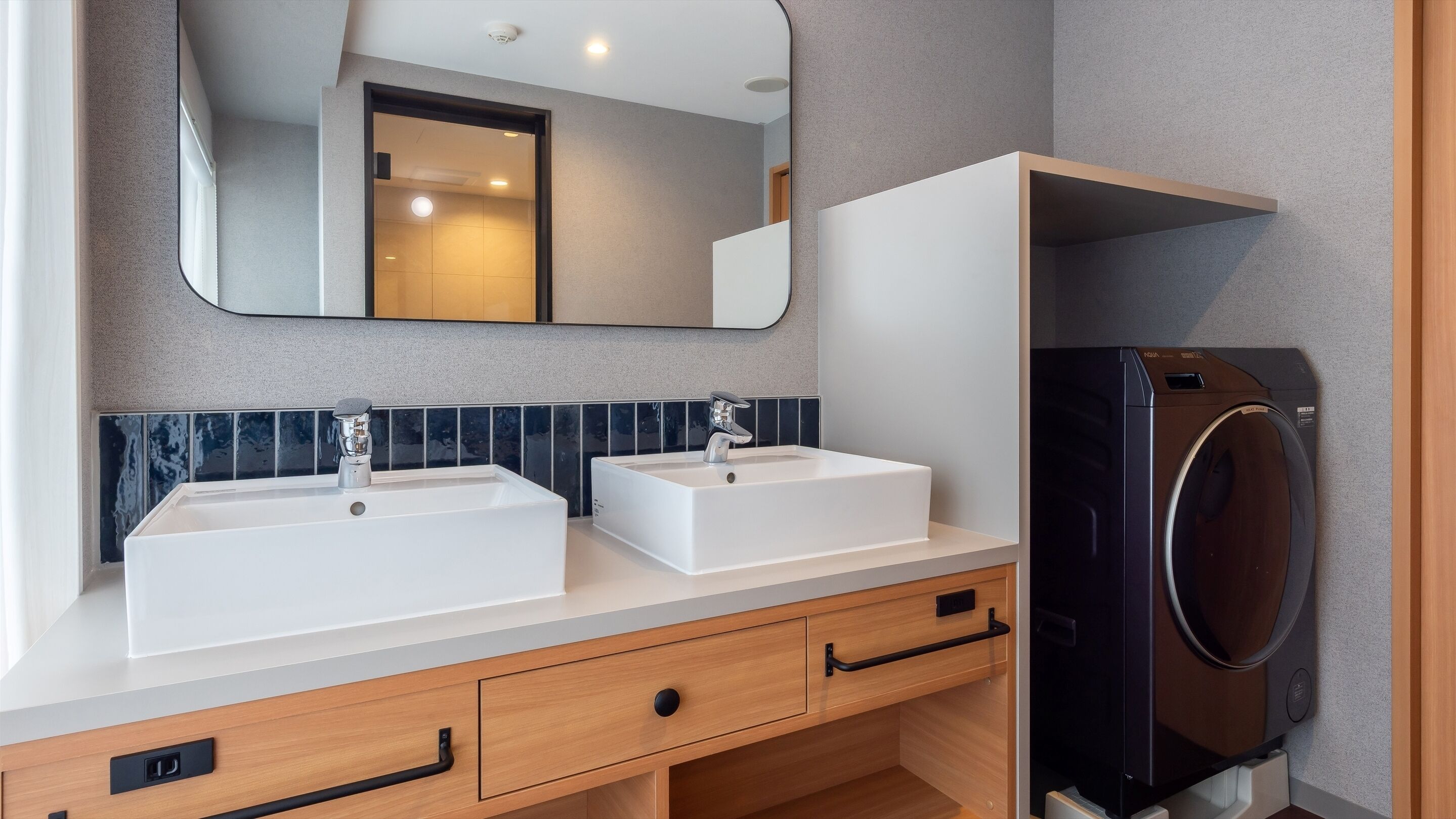 A modern bathroom with two sinks, a mirror, and a built-in washing machine.