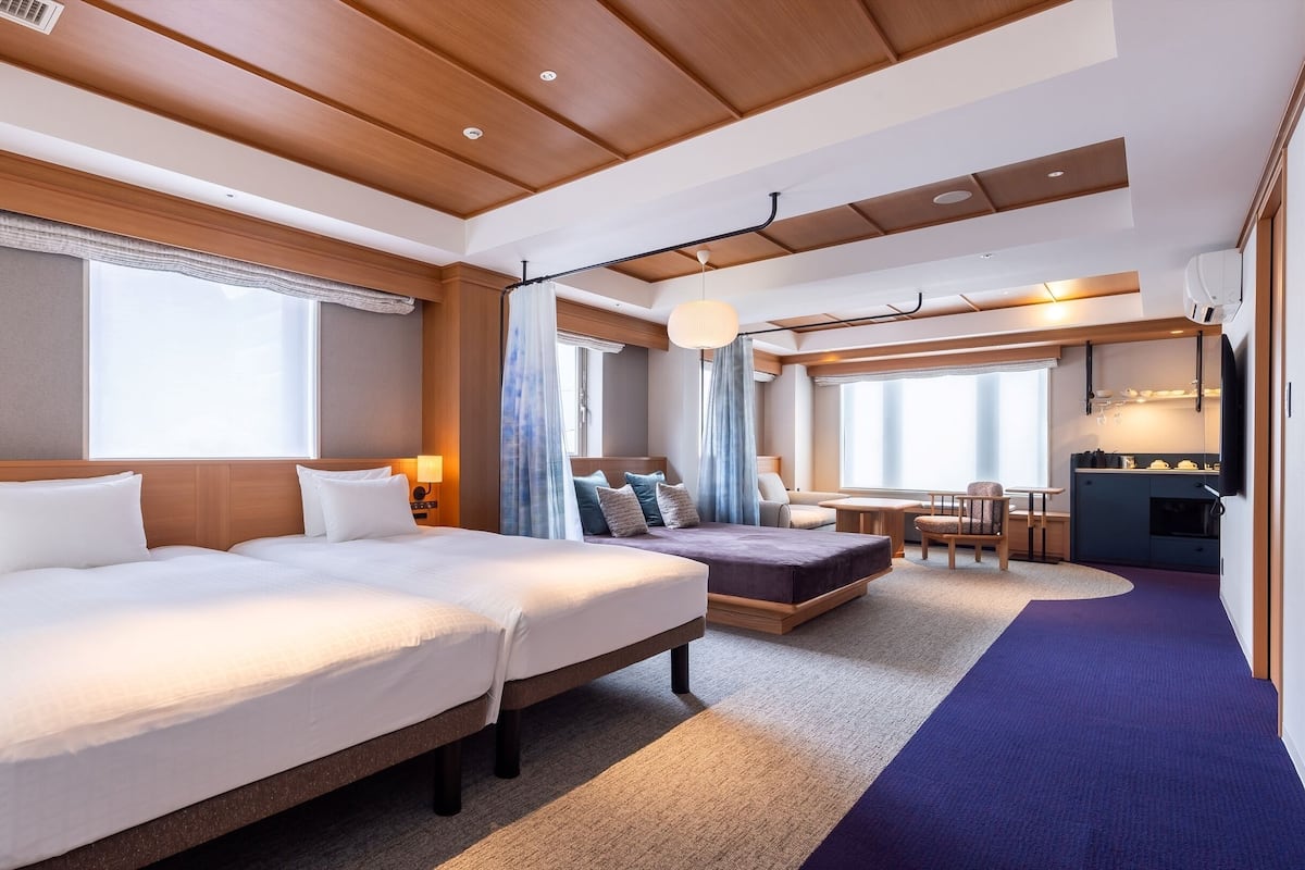 A hotel room with two beds, a dining area, and a kitchenette.