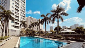 A swimming pool with a tiled edge, surrounded by palm trees and a fence.