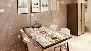 A modern dining area with a marble wall, a long table with a patterned tablecloth, white chairs, and a bicycle-themed pendant light.