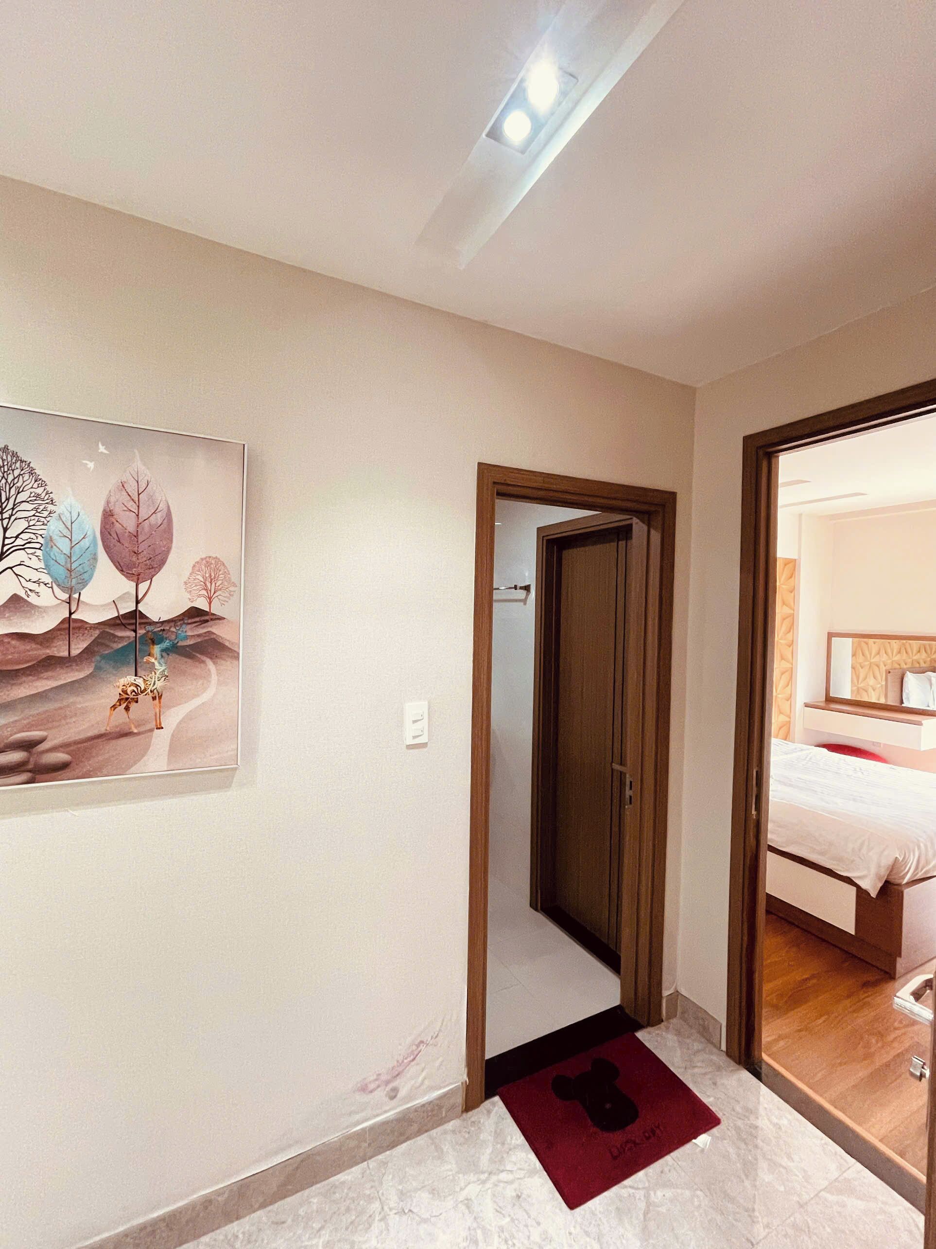 Ein Flur mit einer Holztür, die zu einem Schlafzimmer führt. Ein gerahmtes Kunstwerk befindet sich an der Wand, und eine Fußmatte mit einem Bärenmotiv liegt auf dem Boden.