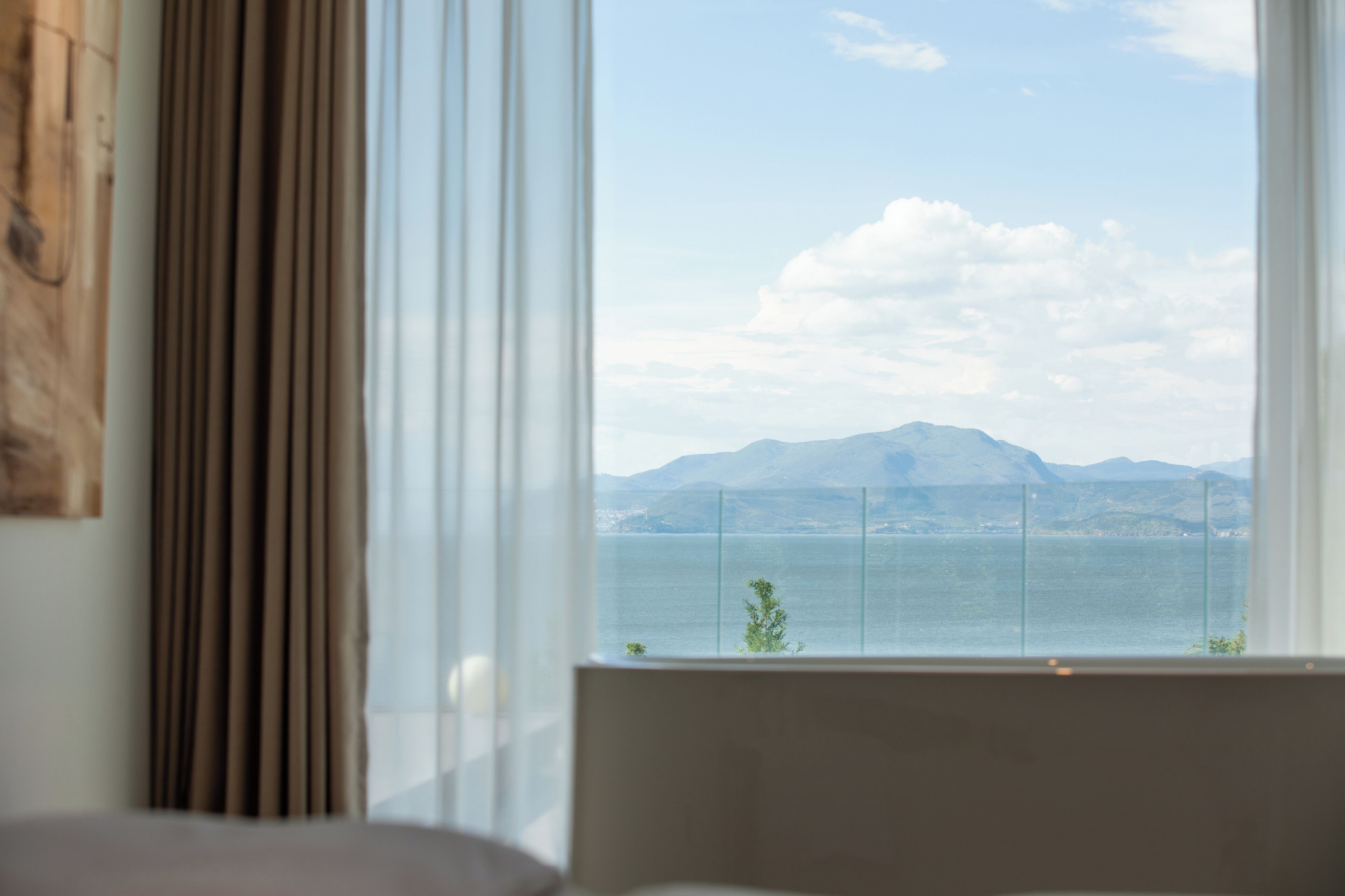 A room with a large window offering a view of a body of water and distant mountains.