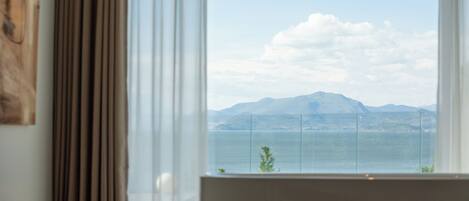 A room with a large window offering a view of a body of water and distant mountains.