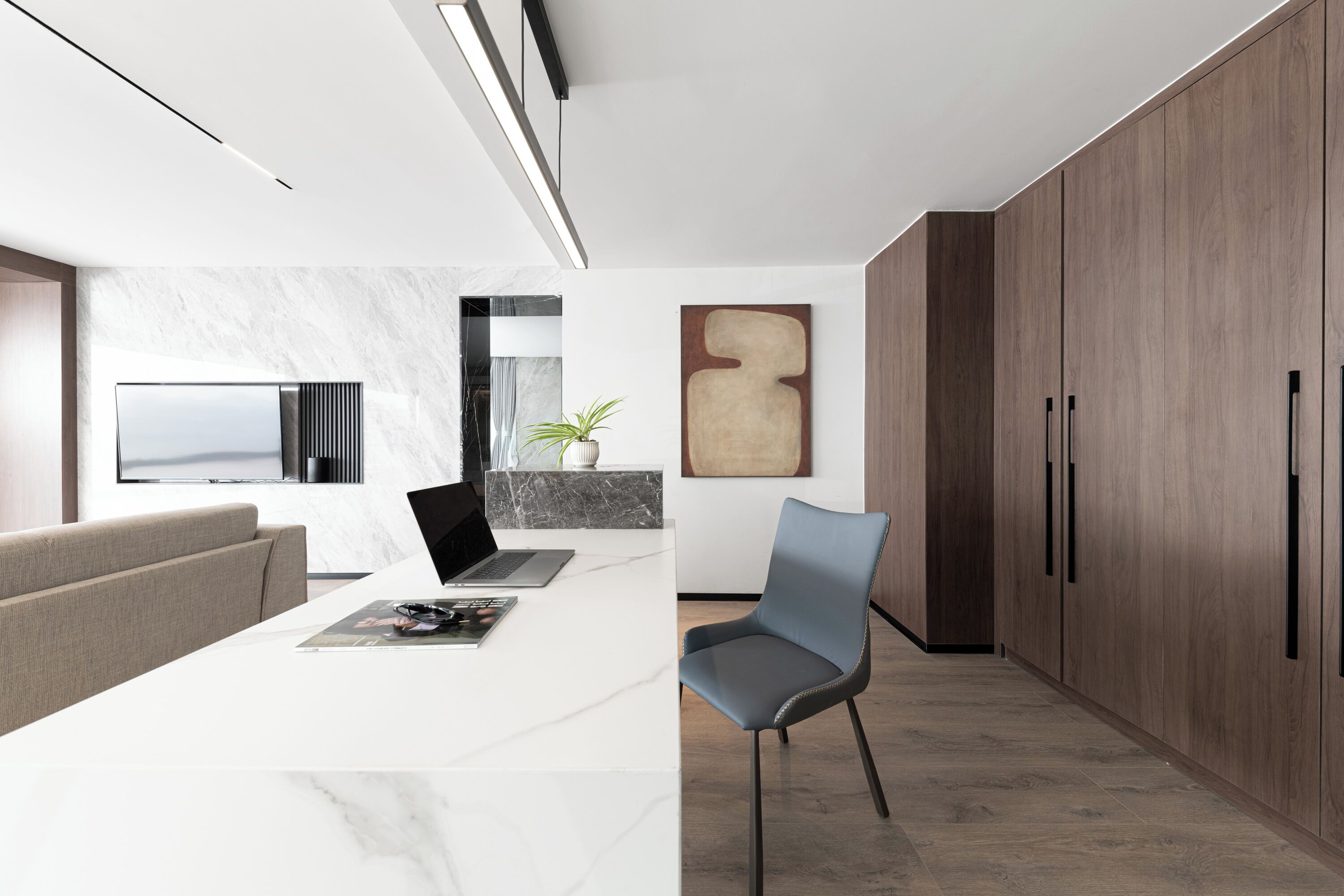 A modern kitchen with a marble countertop, a laptop, a plant, and a large wooden cabinet.