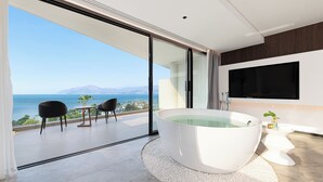 A modern bathroom with a large bathtub, a toilet, and a shower. There is a balcony with a view of the sea and mountains. - Anyu Aranya Collection Sea View Resort Hotel (Dali)