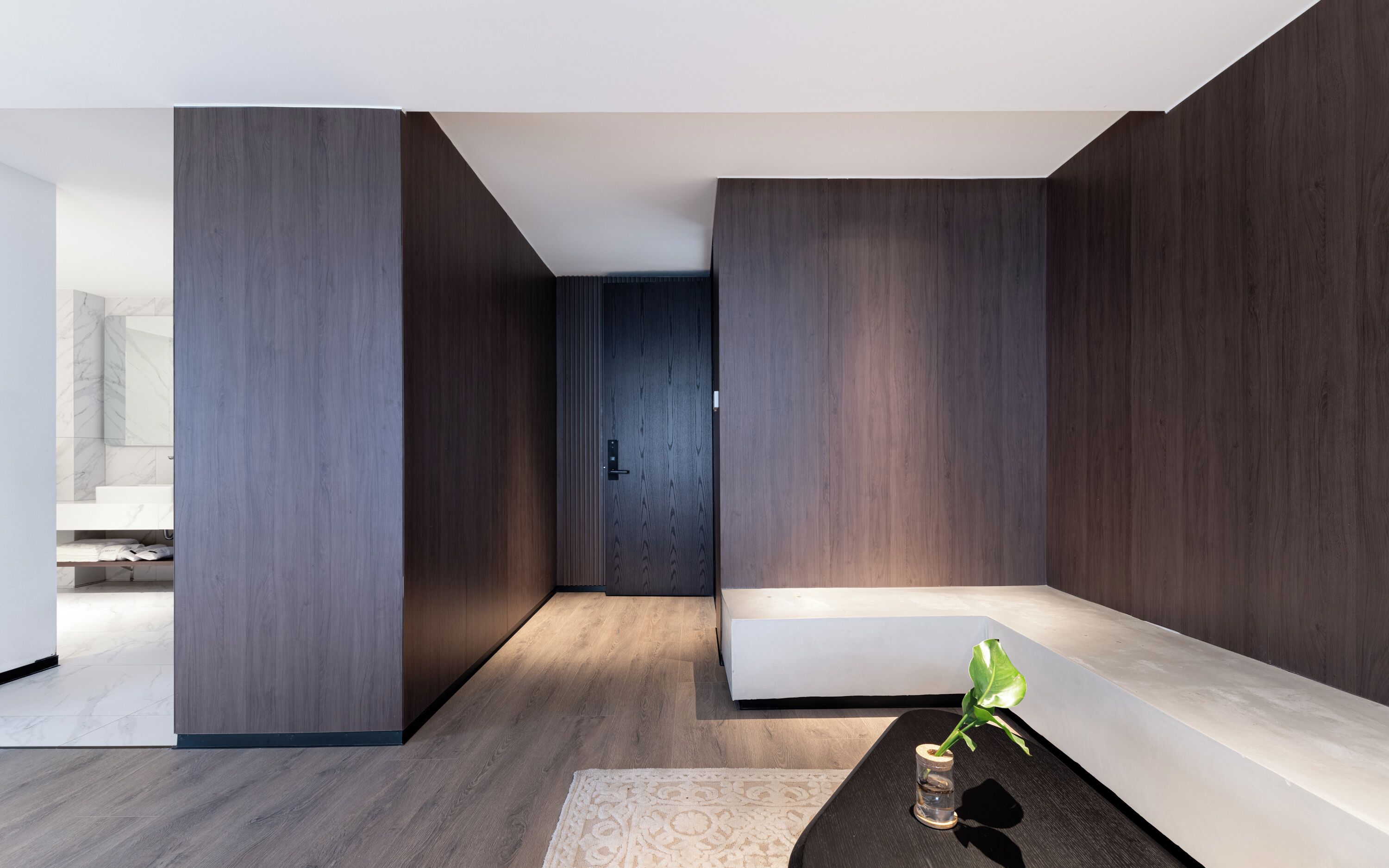 A modern interior with a minimalist design, featuring a wooden floor, a bench, and a small plant on a table.
