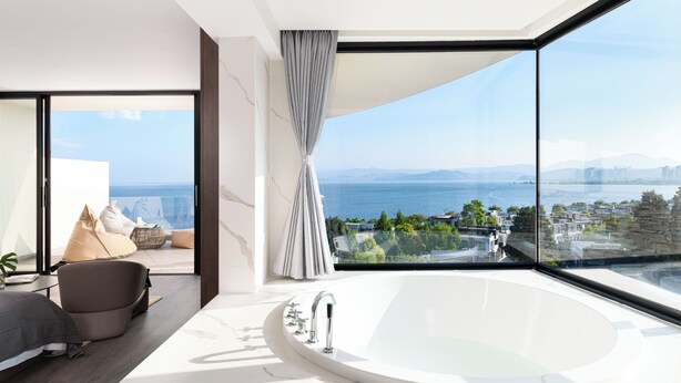 A modern bathroom with a large bathtub, a view of the sea, and a seating area with a sofa and cushions. - Anyu Aranya Collection Sea View Resort Hotel (Dali)