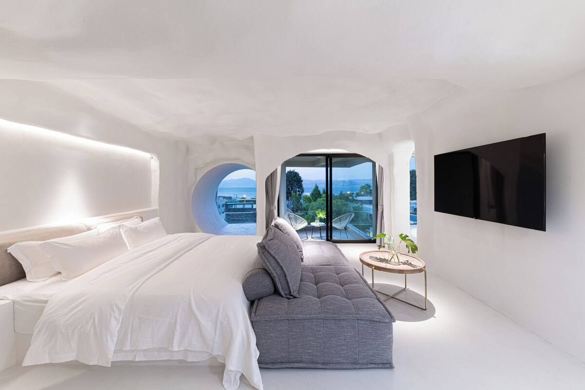 A modern bedroom with a bed, a gray sofa, a round table with a plant, and a TV mounted on the wall.