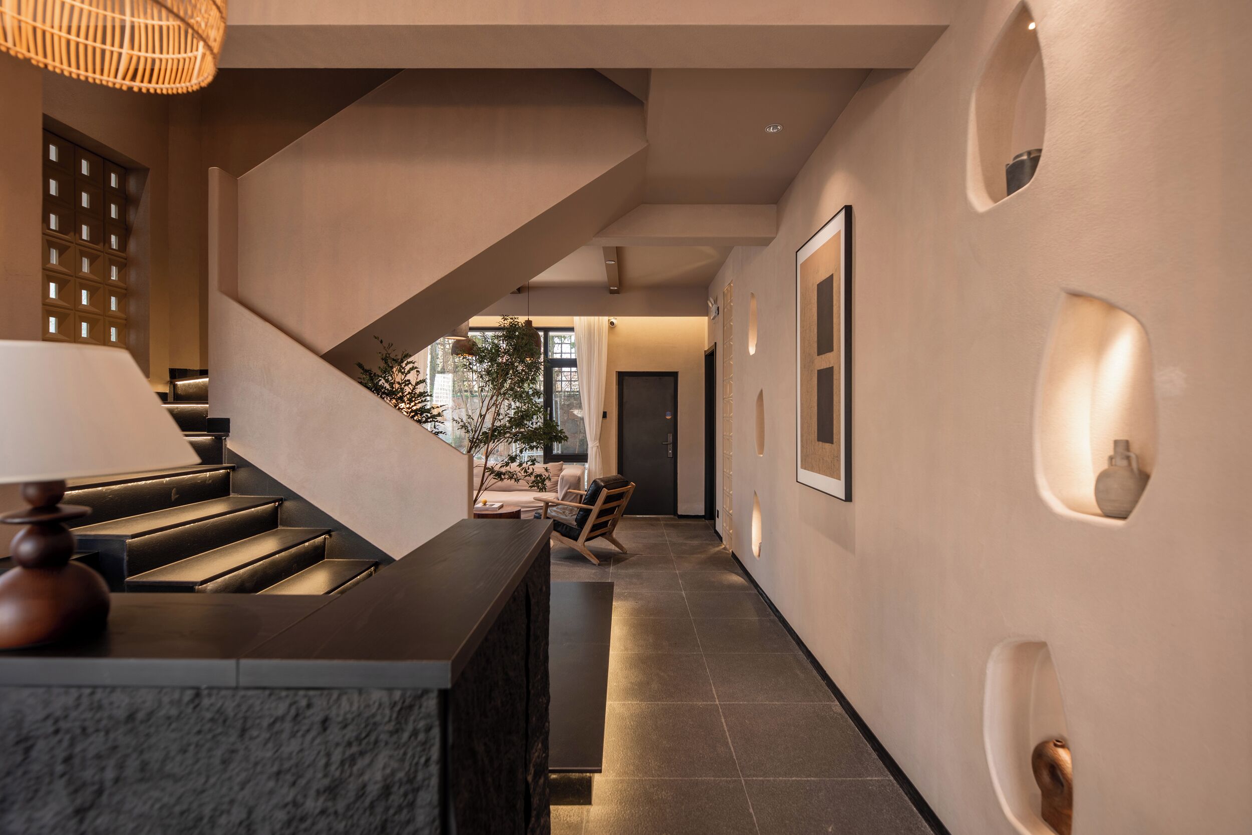 Un interior moderno con una escalera, una recepción y un pasillo que conduce a una zona de estar.
