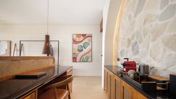A modern kitchen with a stone wall, a wooden dining table with chairs, a hanging pendant light, and a coffee machine.