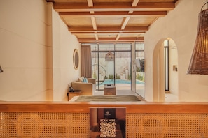 A reception area with a wooden reception desk, a QR code sign, and a view of a pool and outdoor seating area.