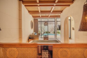 A reception area with a wooden reception desk, a QR code sign, and a view of a pool and outdoor seating area.