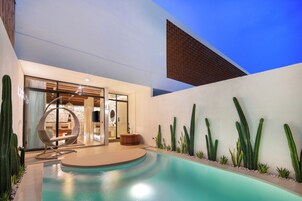 Un espace piscine moderne, doté d’un design circulaire, d’un coin salon avec un fauteuil original, et agrémenté de différentes espèces de cactus le long du bord de la piscine.