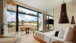 Una habitación de hotel moderna con una cama grande, un área de descanso con una mesa y sillas, una bañera y ventanas amplias con vistas al exterior.