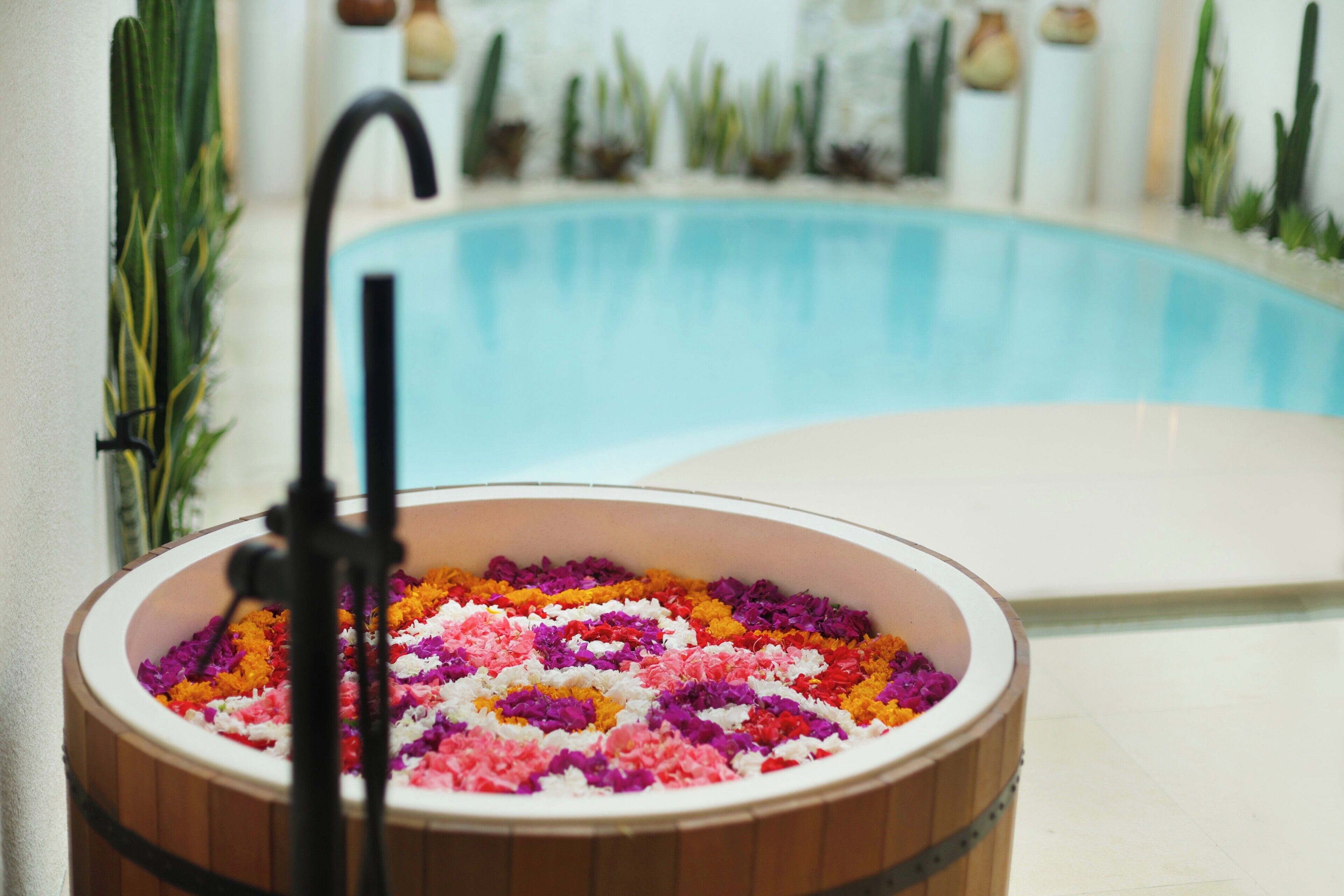 A wooden tub filled with colorful flower petals, a black stand, and a pool in the background.