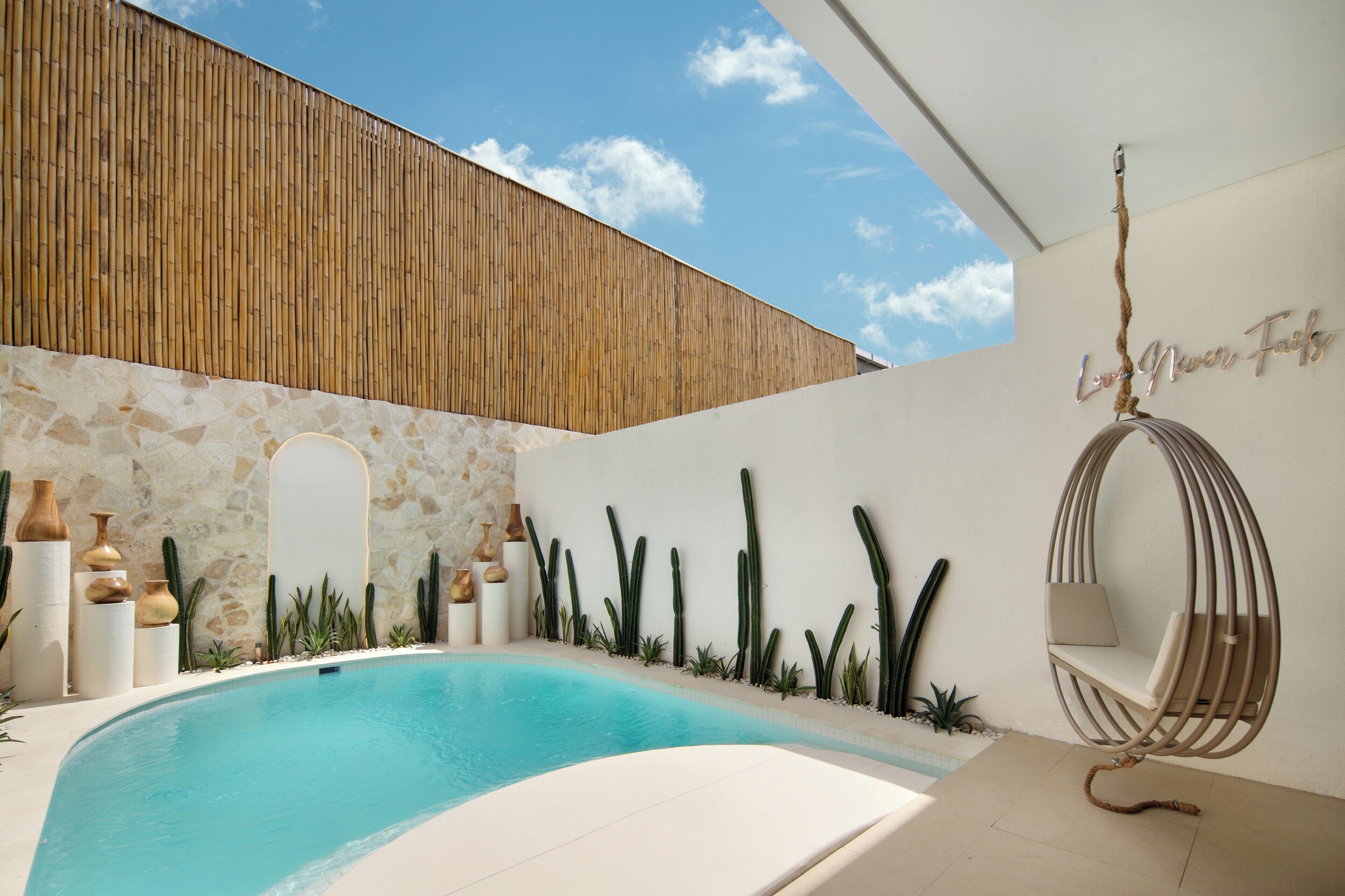 Un área de piscina moderna con una hamaca colgante, cactus y un muro de piedra.