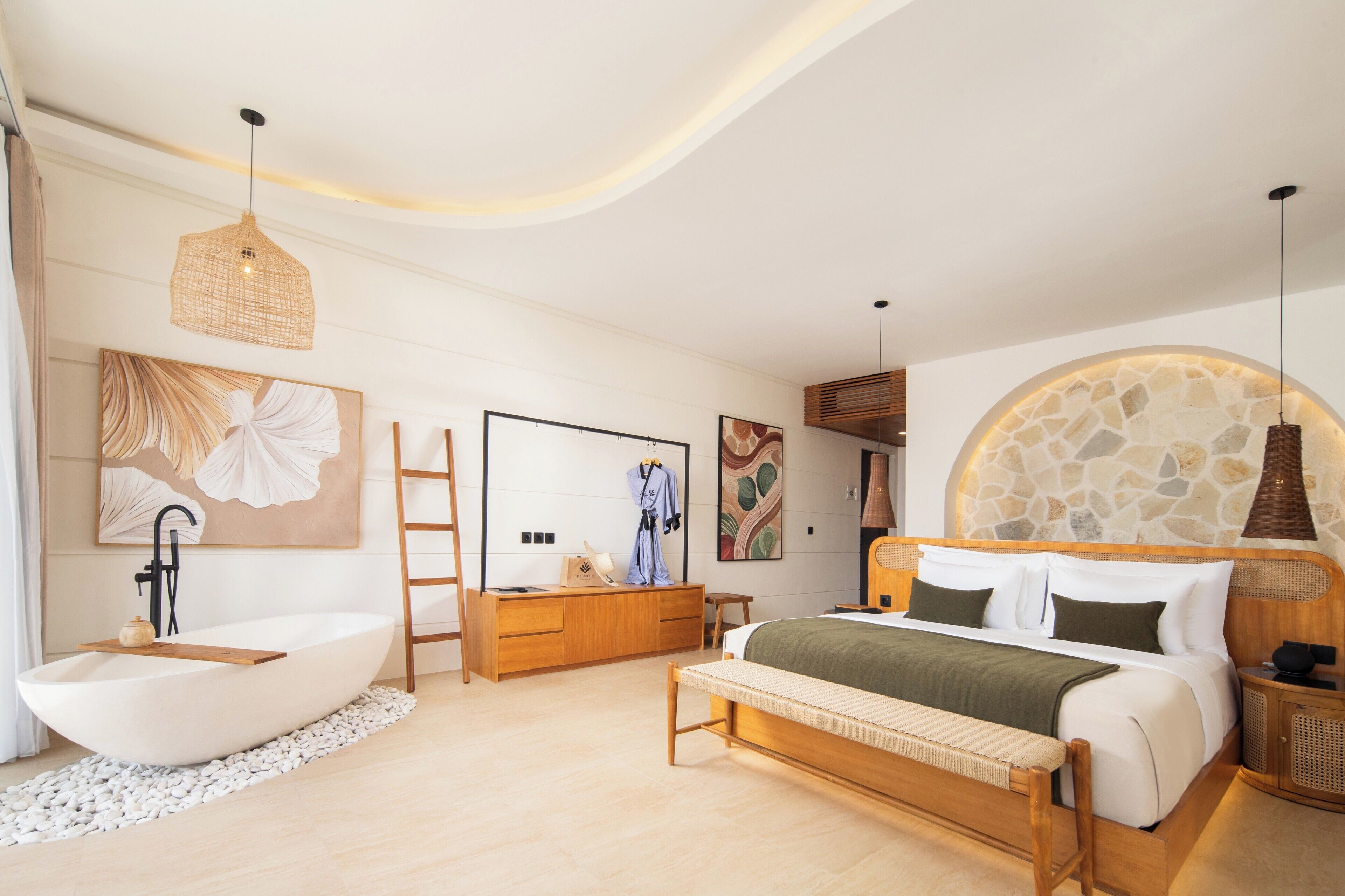 A modern bedroom with a large bed, a bathtub, a wooden bench, and a stone wall.