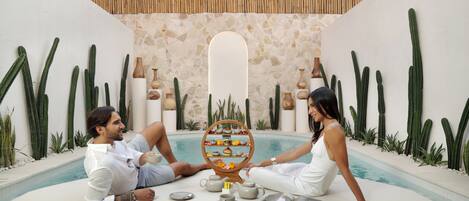 A couple relaxing by a pool with a tea set and a decorative mirror.