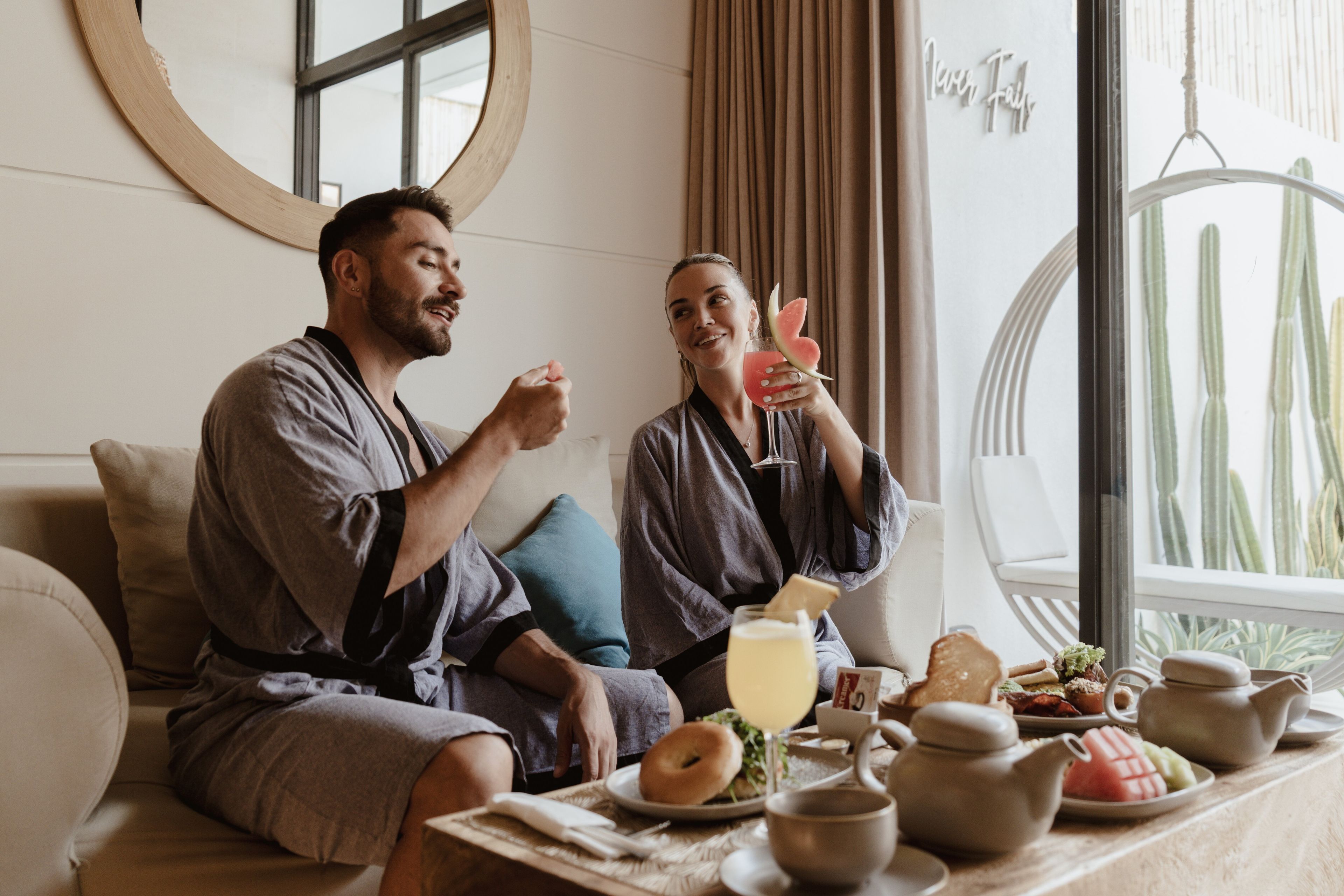 Dos personas sentadas en un sofá en una habitación con una mesa de comedor dispuesta con comida y bebidas.