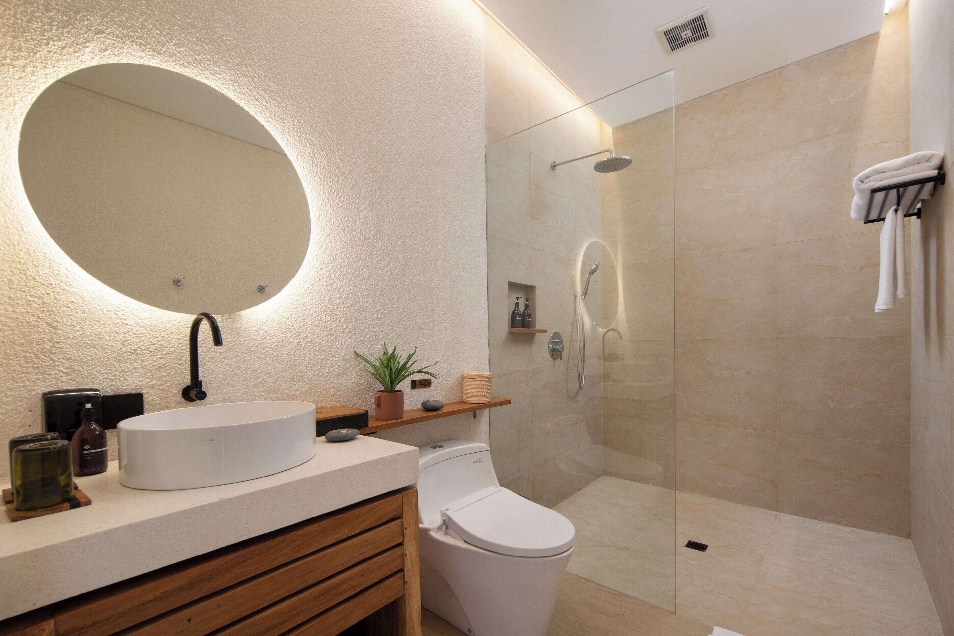 Un baño moderno con un espejo redondo, un lavamanos, un inodoro y una zona de ducha con mampara de vidrio.