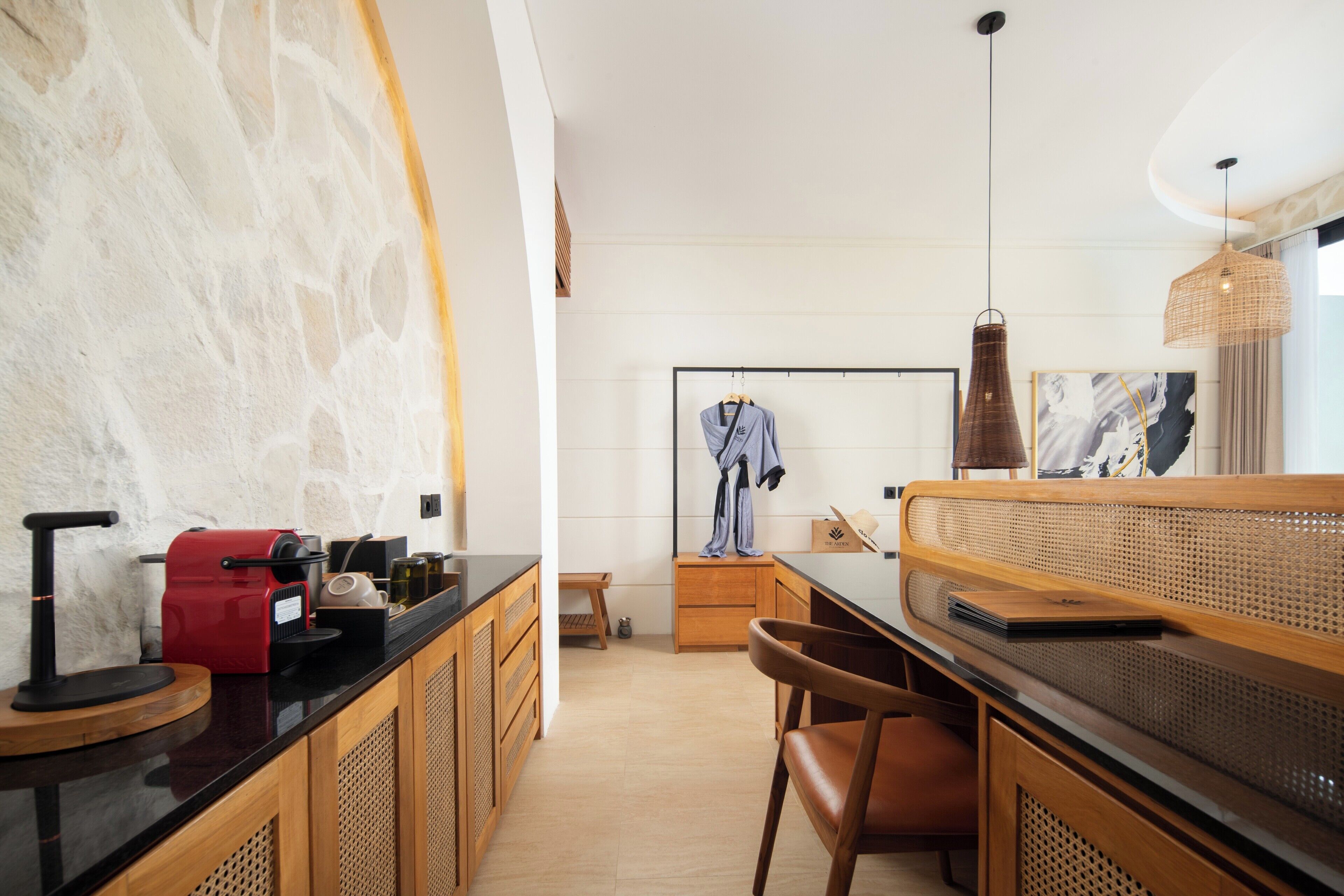 A modern kitchen with a black countertop, wooden cabinets, a red coffee machine, and a hanging robe.