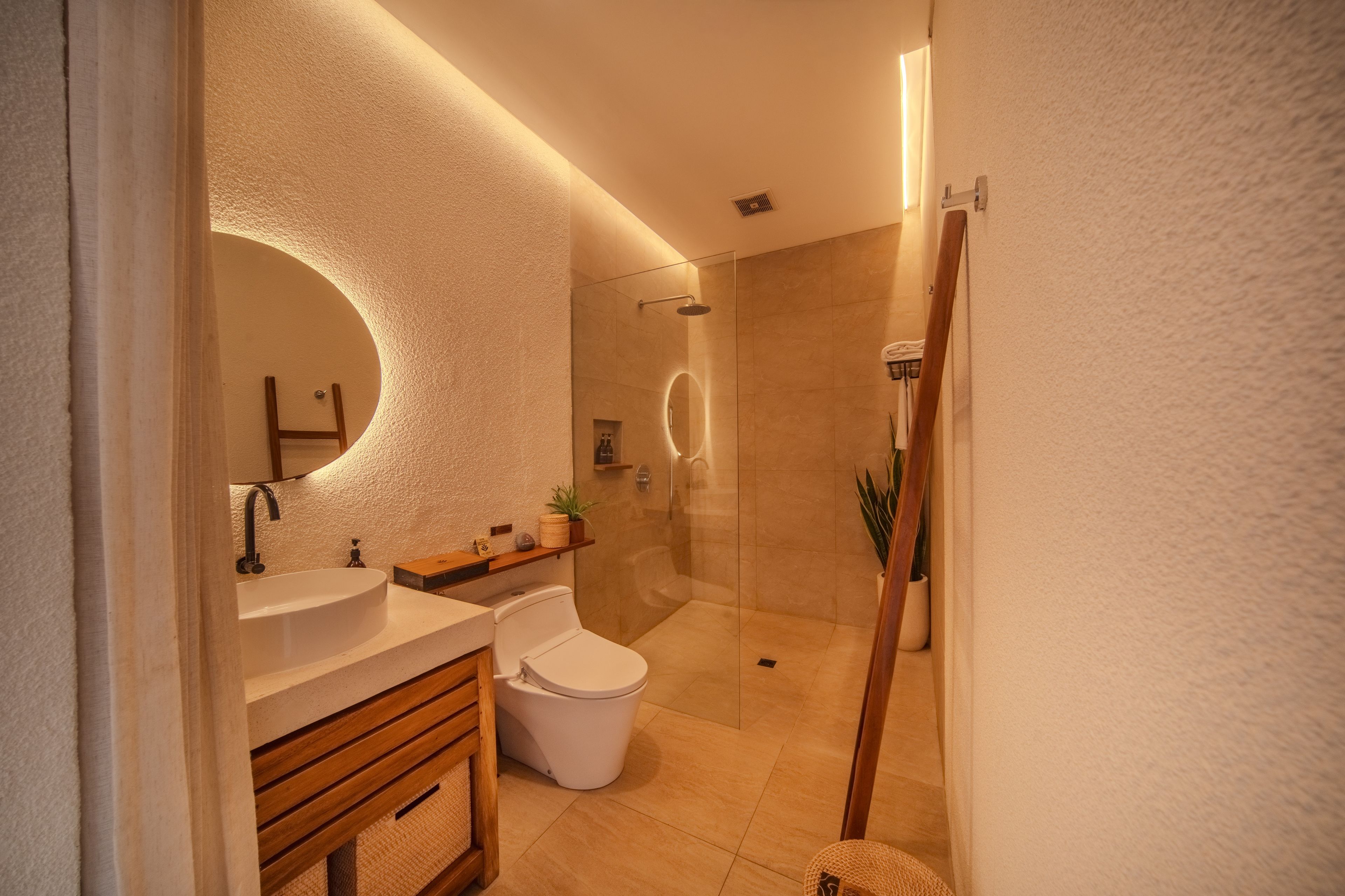 Un baño moderno con un espejo redondo, lavamanos dobles, inodoro y zona de ducha con mampara de vidrio.