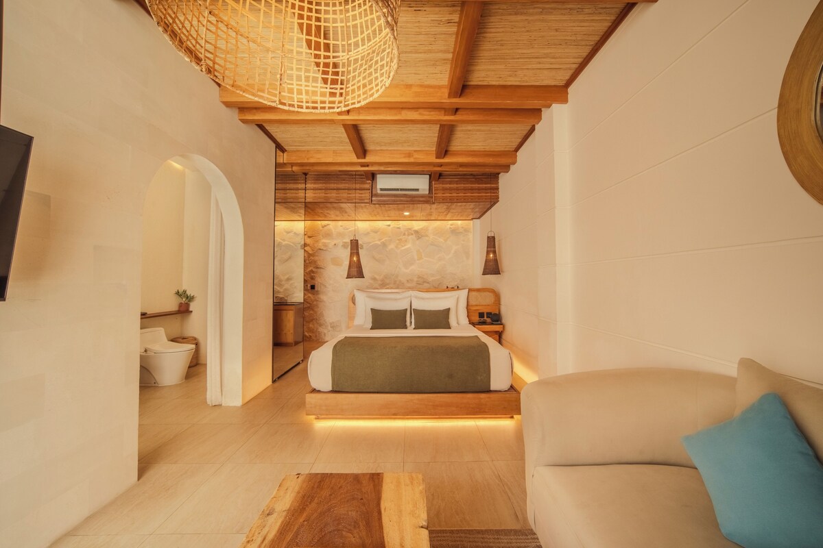 Una camera d'albergo moderna con soffitto in legno, un letto con biancheria bianca, un comodino in legno e un piccolo tavolo con una lampada.