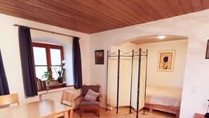 Una habitación con techo de madera, una mesa de comedor con sillas, un sofá, una cama y una ventana con cortinas.