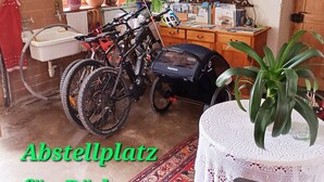 Una habitación con una bicicleta, una mesa con mantel de encaje y una alfombra estampada.