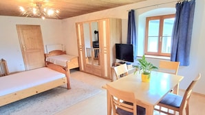 Una habitación con cama, armario, televisor, mesa con sillas y ventana con cortinas.