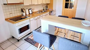 Cocina compacta con gabinetes blancos, horno empotrado, pileta y comedor para dos personas.