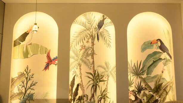 Una pared con tres ventanas arqueadas, cada una con un mural tropical de aves y follaje.