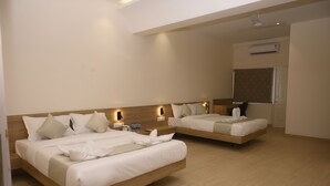 Habitación de hotel con dos camas, cabecero de madera, mesitas de noche con lámparas, unidad de aire acondicionado y una pizarra en la pared.