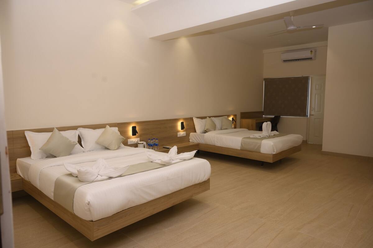 Habitación de hotel con dos camas, cabecero de madera, mesitas de noche con lámparas, unidad de aire acondicionado y una pizarra en la pared.