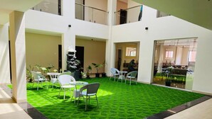 Un espacio interior amplio con piso de césped artificial verde, sillas blancas y una escalera que sube a un nivel superior.