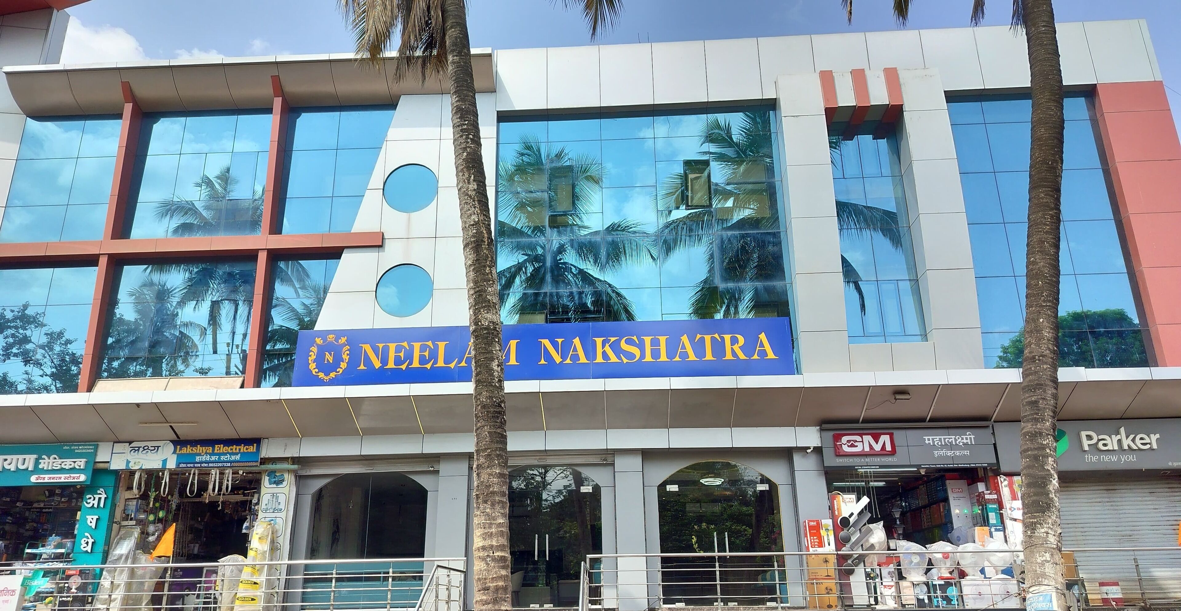 A building with a sign reading "Neelam Nakshatra" and various shops including "Lakshmi Electrical" and "GM".