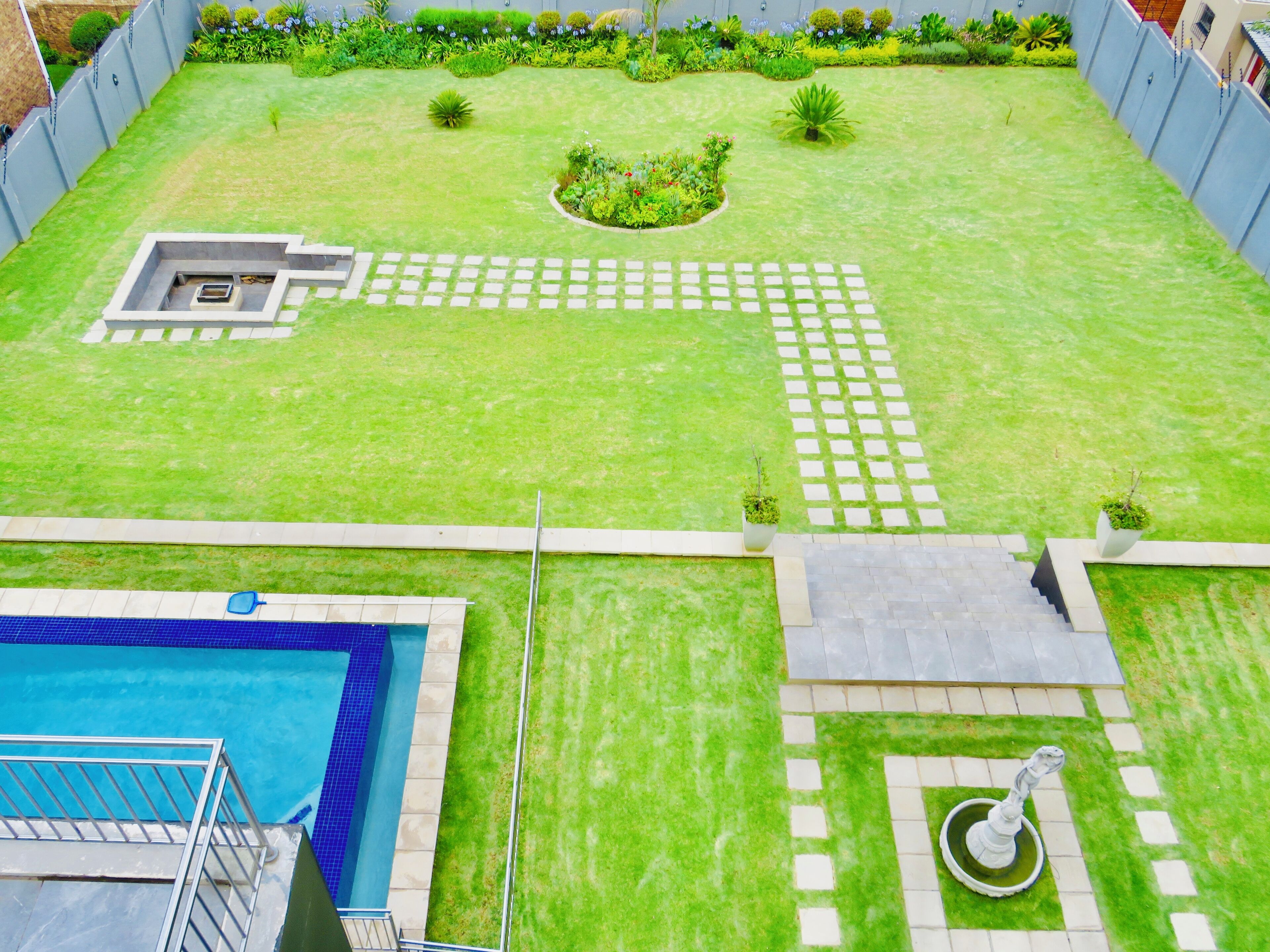 Ein Garten mit Schwimmbad, Brunnen und gepflegtem Rasen mit einer Blumenrabatte.
