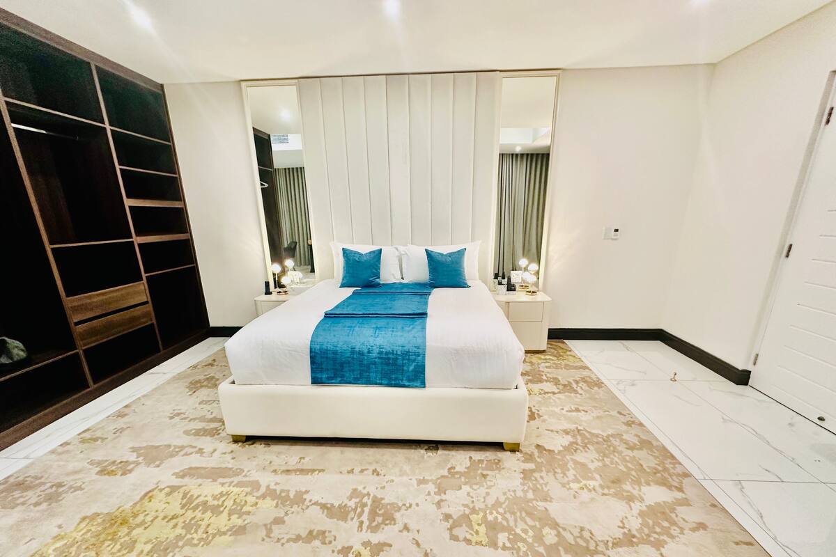 A modern bedroom with a large bed, a vanity with lights, and a walk-in closet.