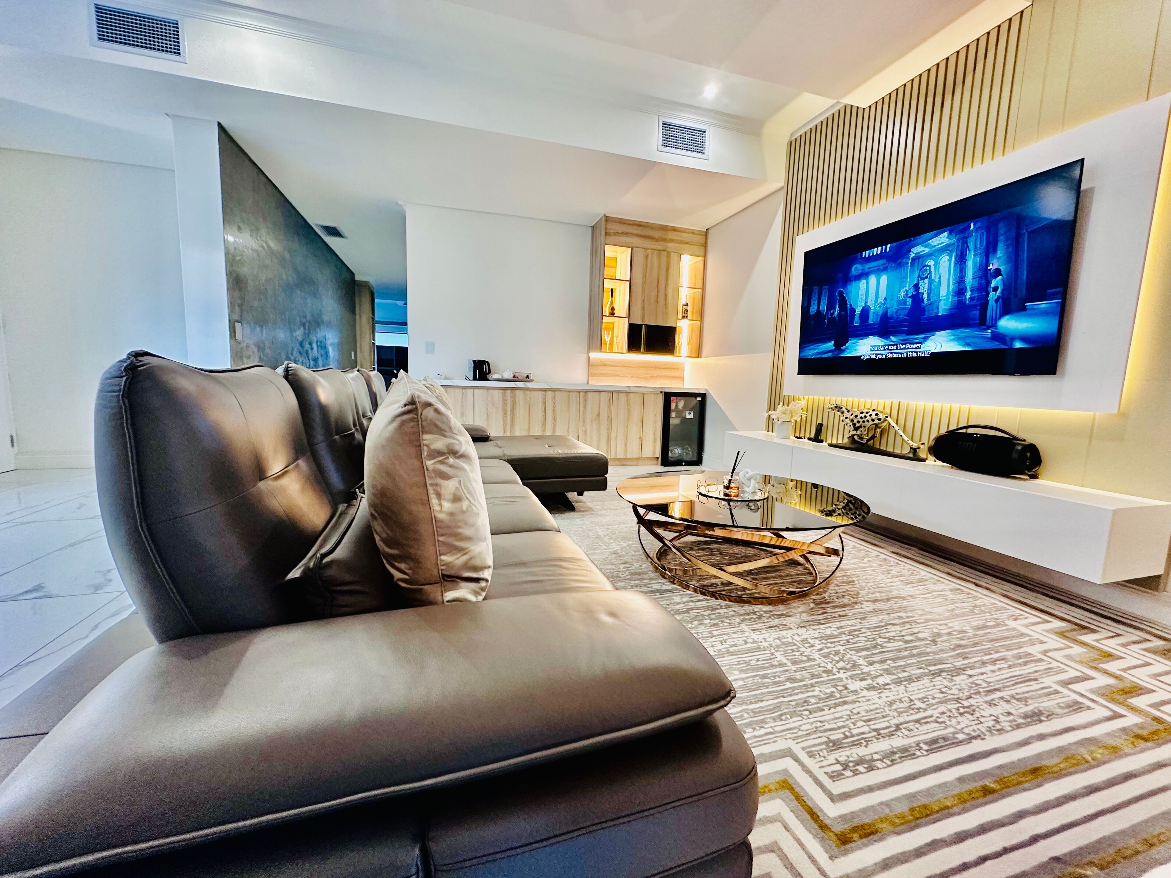 A modern living room with a leather sofa, a coffee table, and a flat-screen TV mounted on the wall.