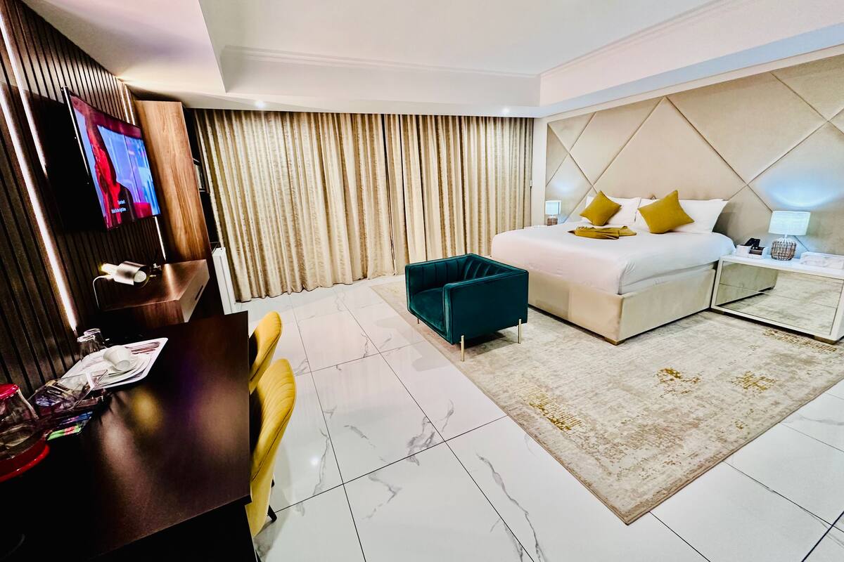 A modern hotel room with a large bed, a desk with a chair, a television, and a decorative mirror.