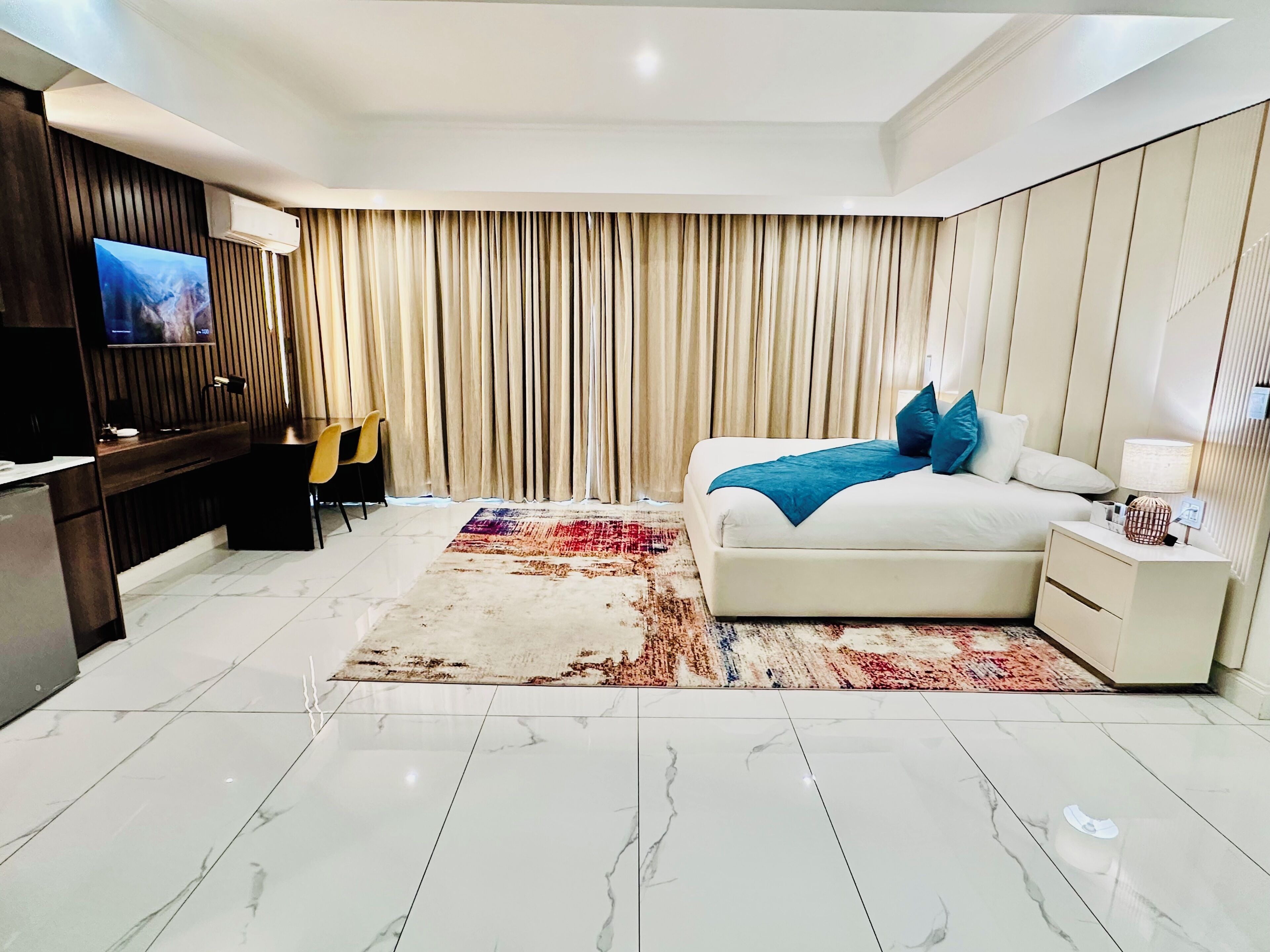 A modern hotel room with a large bed, a flat-screen TV, a desk, and a chair.