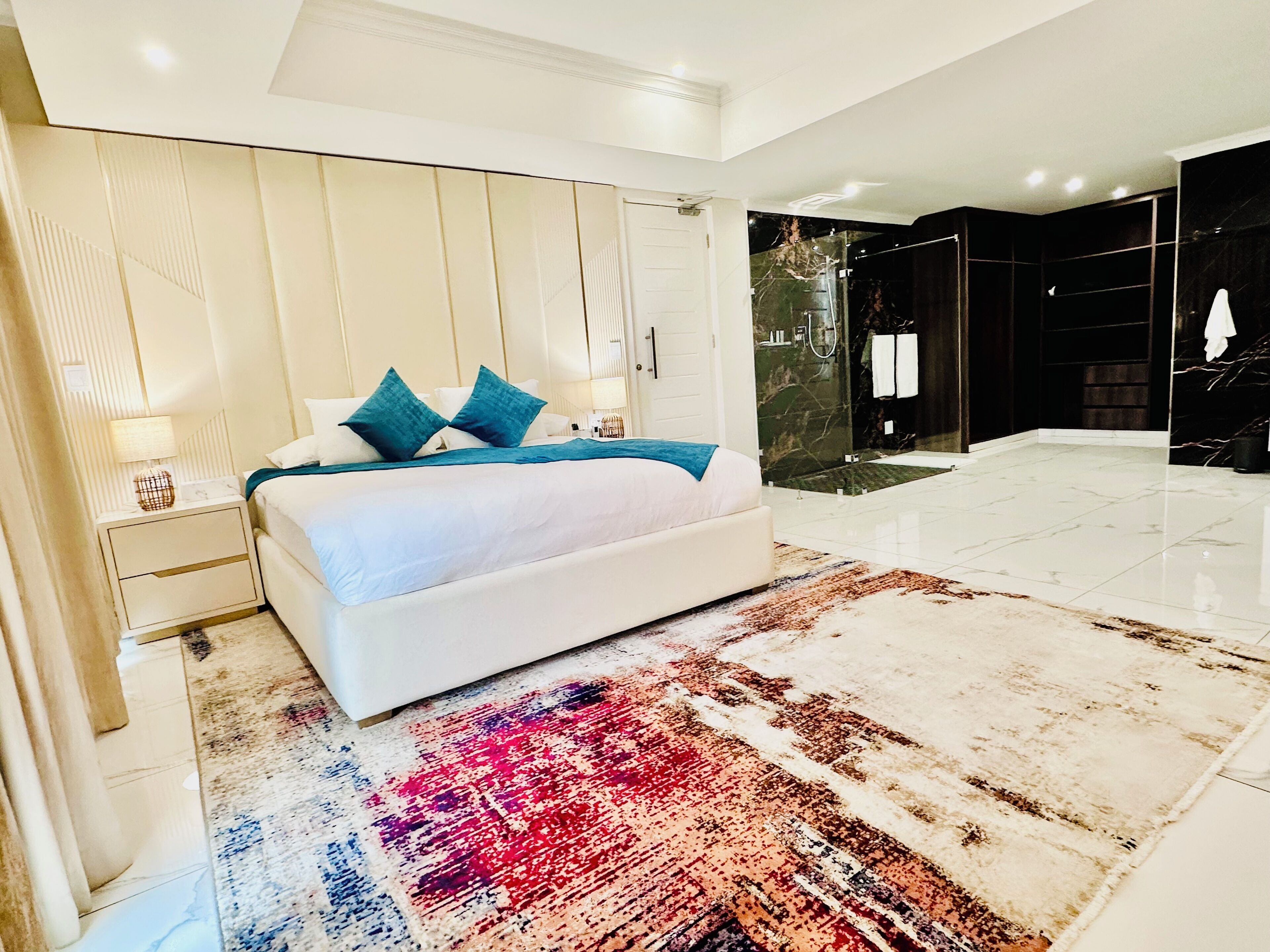 Una camera da letto moderna con un letto grande, un tappeto decorato e un bagno con doccia in vetro.